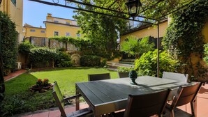 Une terrasse avec une table et des chaises, entourée de verdure et offrant une vue sur les bâtiments.