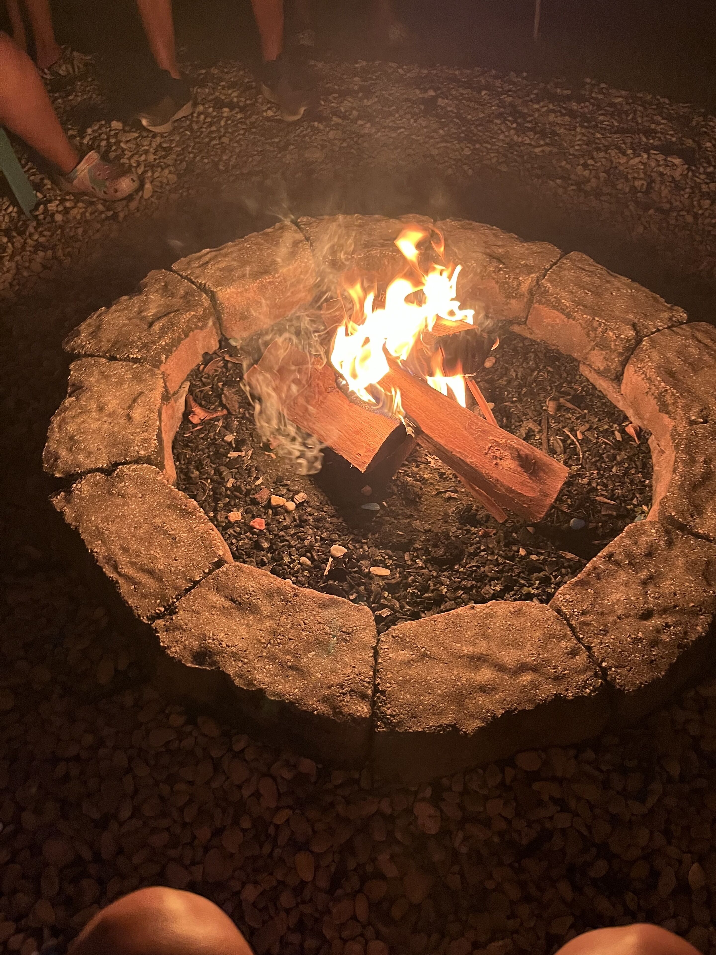 Un hogar de piedra con leña encendida, rodeado por una zona de grava.