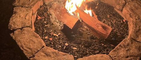 Un hogar de piedra con leña encendida, rodeado por una zona de grava.