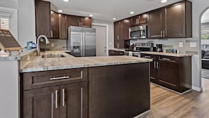 A modern kitchen with dark wood cabinets, stainless steel appliances, and a marble countertop. - Lakehouse Living w/ Firepit and Boat Dock to relax and Enjoy the Sunset (palm harbor)
