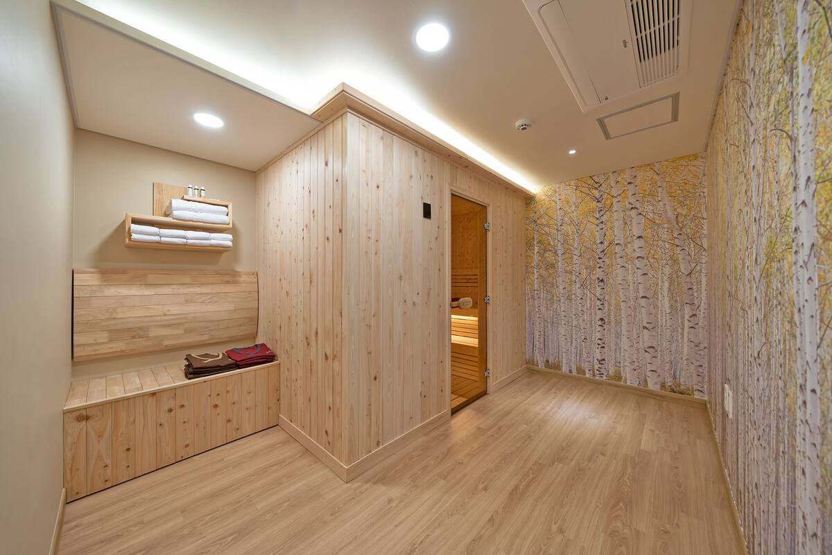 A wooden room with a bench, shelves, and a door leading to a bathroom.