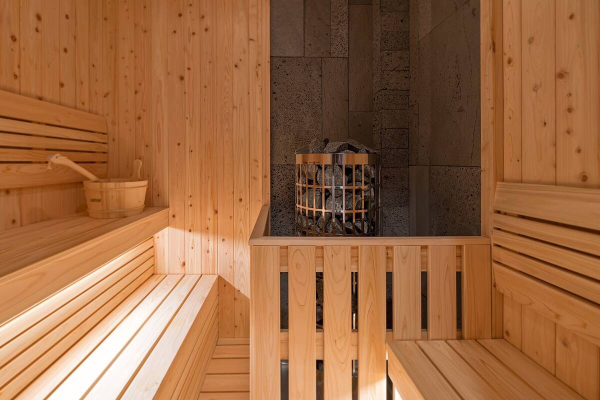 A wooden sauna with benches, a stone wall, and a metal container with rocks.