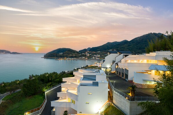 A modern hotel with a waterfront view, featuring a curved building design and a well-lit entrance.