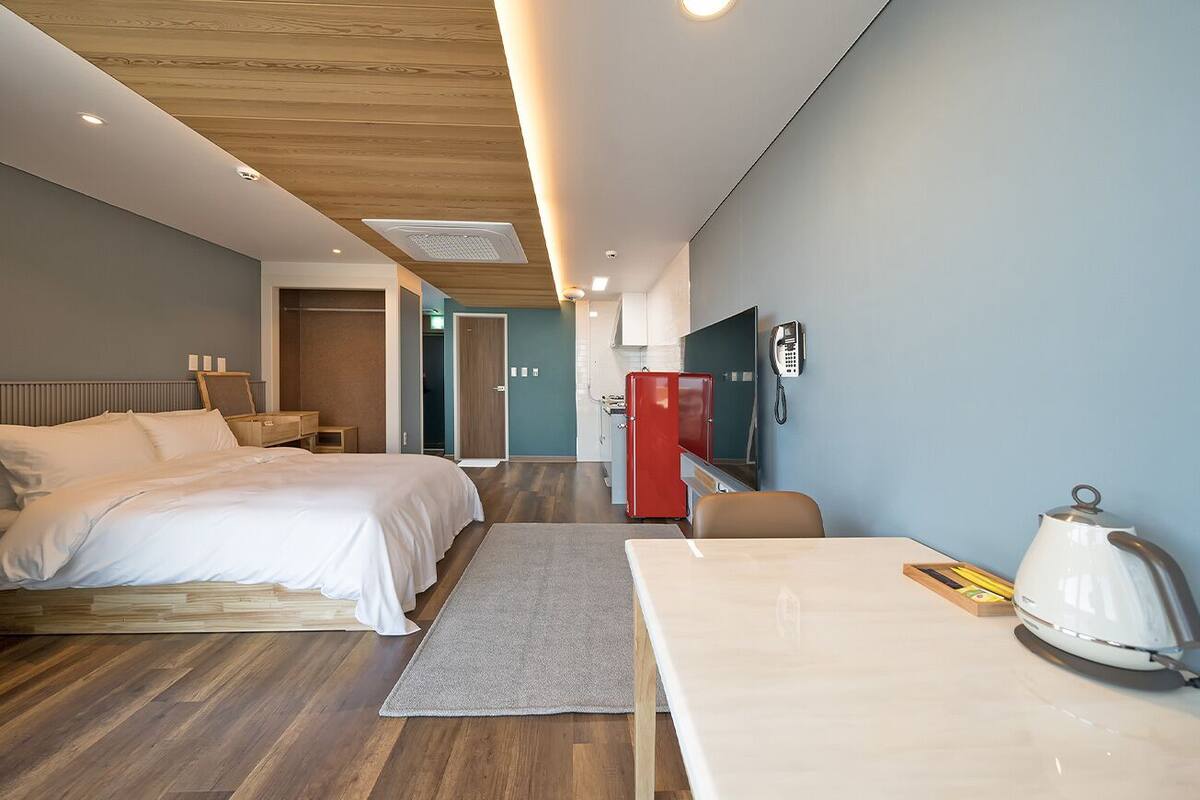 A modern hotel room with a bed, a desk, a kettle, and a TV.