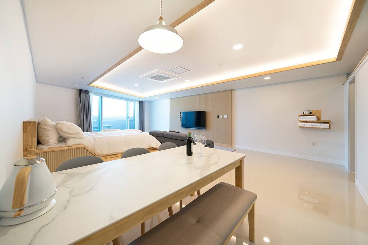 A modern hotel room with a large bed, a dining table, a sofa, and a TV mounted on the wall.
