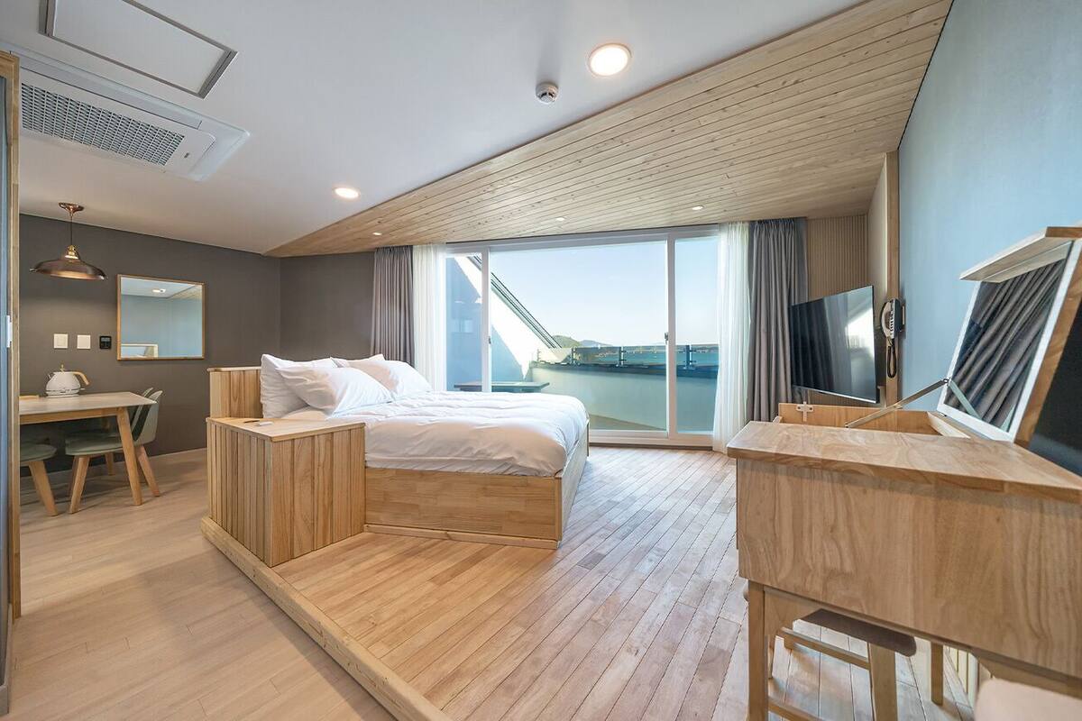 A modern hotel room with a wooden bed, a desk, and a large window offering a view of a bridge.