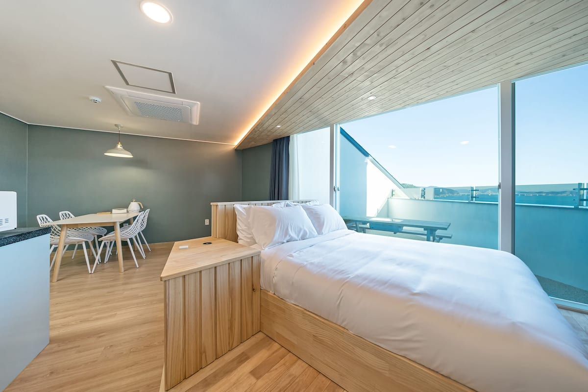 A modern hotel room with a wooden bed, a desk, and chairs, a large window with a view of the city.