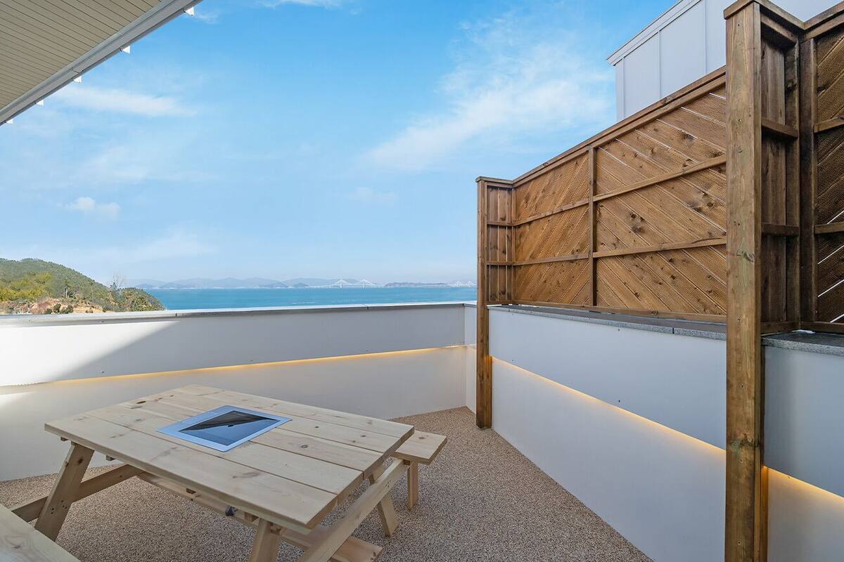 A wooden deck with a table and bench, overlooking a scenic view of the sea and hills.