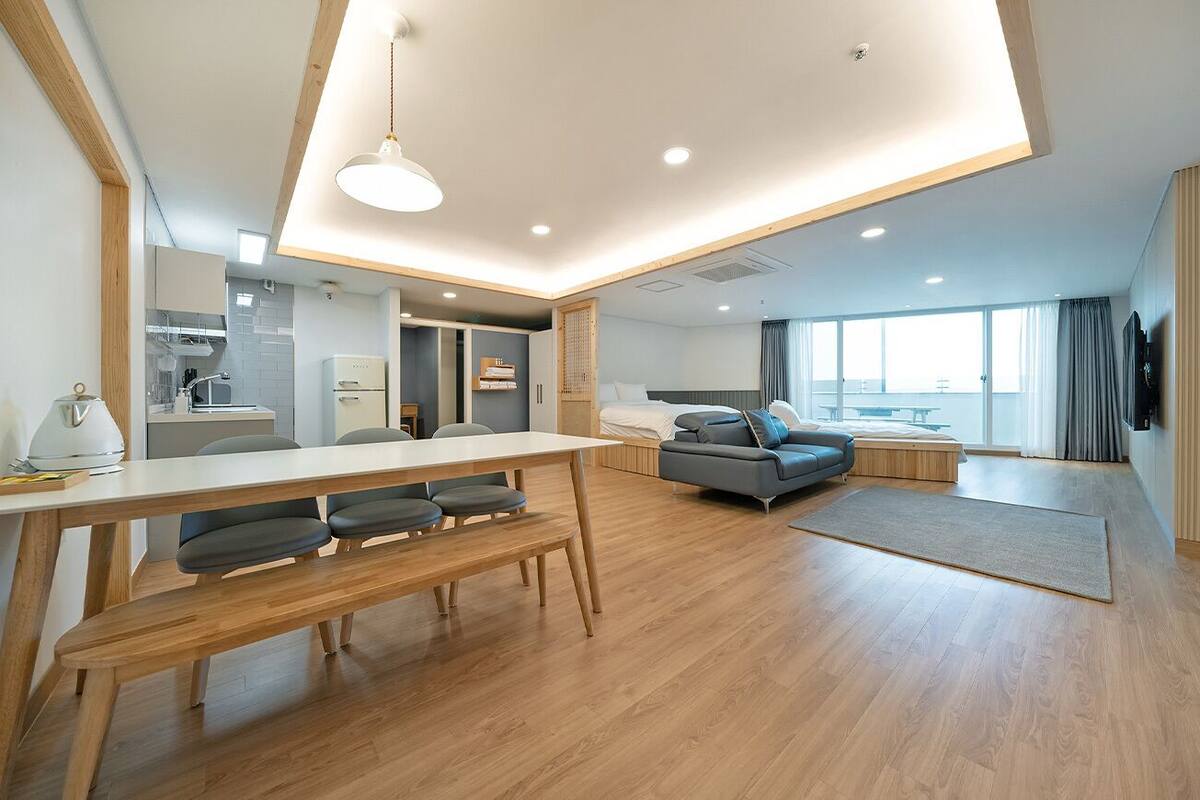 A modern living room with a wooden dining table, a sofa, and a large window.