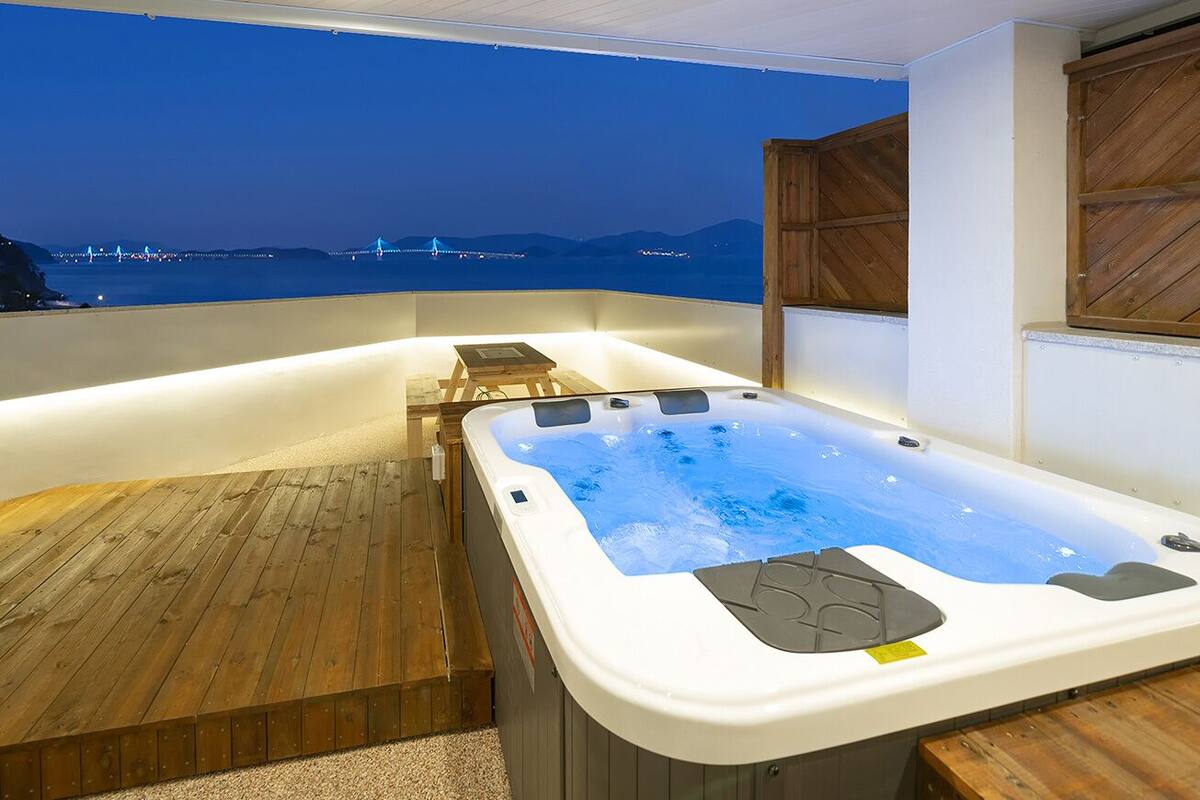 A hot tub on a balcony with a view of a bridge and mountains.
