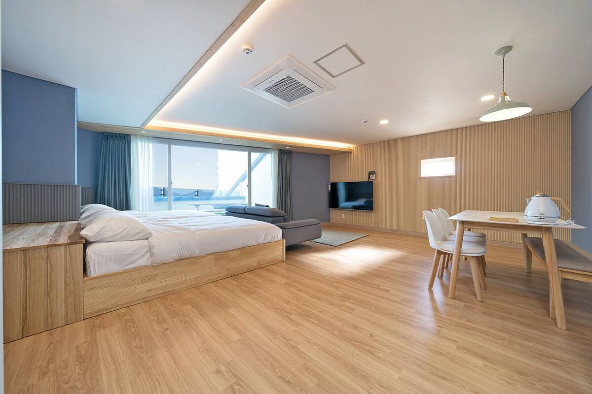 A modern hotel room with a wooden floor, a bed with white linens, a desk with a chair, and a television.