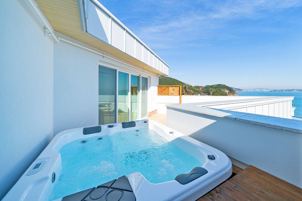 A modern balcony with a hot tub, glass doors, and a view of the sea.