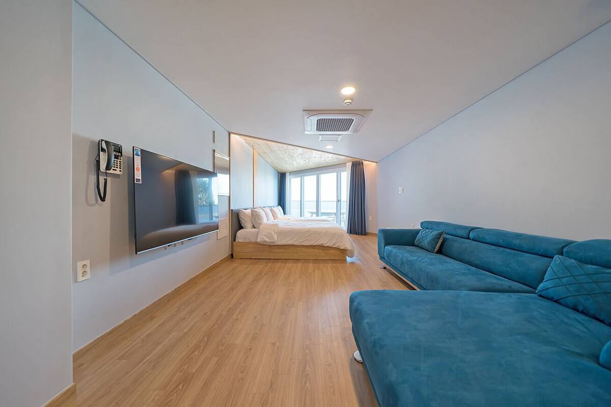 A modern hotel room with a large bed, a blue sofa, a flat-screen TV, and a phone on the wall.