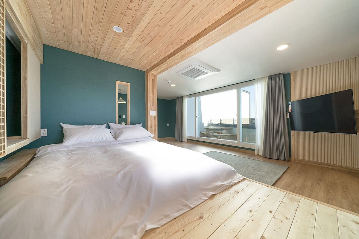 A bedroom with a large bed, wooden ceiling, and a TV on the wall.