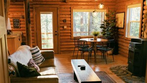 Ein gemütliches Holzblockhaus-Interieur mit Sofa, Esstisch, Stühlen und Kamin.