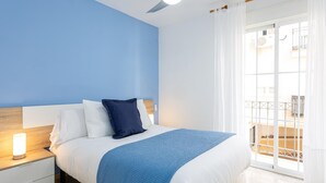 Une chambre avec un lit, une table de chevet, un ventilateur de plafond et une vue sur un balcon.