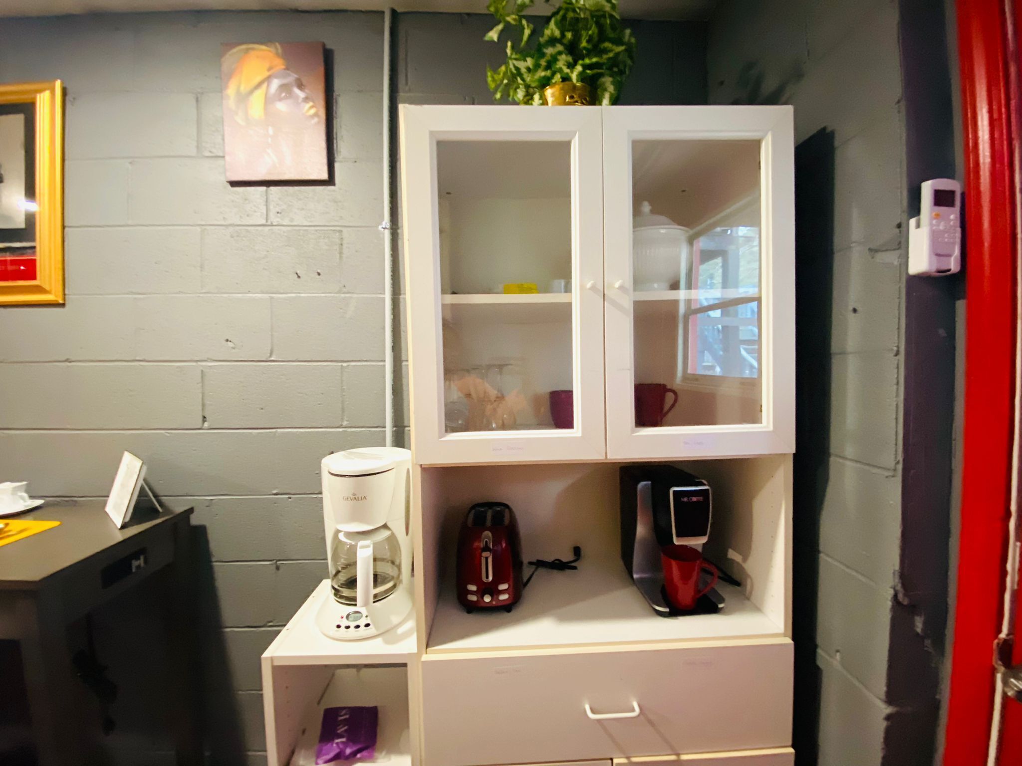 Eine Küchenzeile mit Kaffeemaschine, Toaster und einem kleinen Schrank mit Glastüren.