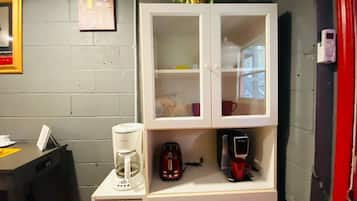 Eine Küchenzeile mit Kaffeemaschine, Toaster und einem kleinen Schrank mit Glastüren.