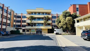 A multi-story building with a 'UNITING' sign, parking lot, and several parked cars. - 1 BR apartment at Glenelg Moseley (Glenelg)