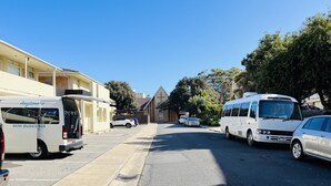 A street with parked vehicles, including a white van and a bus, and a building with a cross on the roof. - 1 BR apartment at Glenelg Moseley (Glenelg)