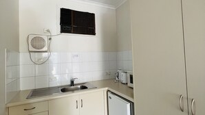 A compact kitchen with white cabinets, a built-in microwave, a small sink, and a window with blinds. - 1 BR apartment at Glenelg Moseley (Glenelg)
