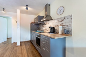 Une cuisine moderne avec des armoires grises, un plan de travail en bois, une hotte de cuisinière en acier inoxydable, une machine à café et une horloge au mur.