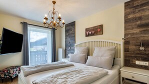 Ein Schlafzimmer mit einem großen Bett, einer Chandelier, einem Flachbildfernseher, einer Wand mit Holzverkleidung und Blick ins Freie.