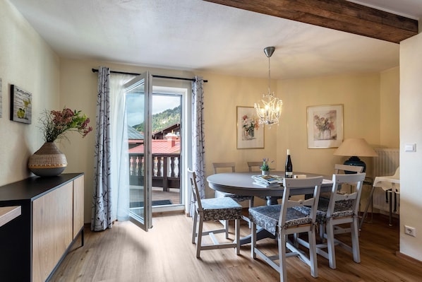 Un coin repas avec une table ronde, des chaises, un lustre et une vue à travers une porte vitrée.