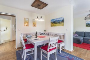 A dining area with a white table and chairs, a wooden ceiling, and a red rug.