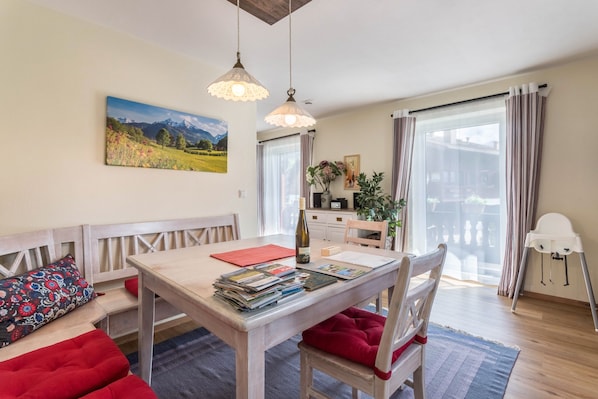 A dining area with a wooden table, red cushioned seating, a painting of a landscape, and a bottle of wine.