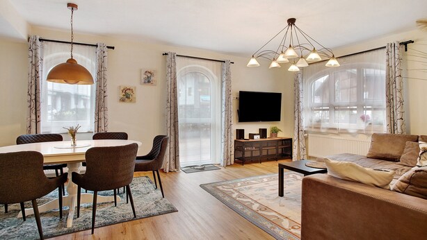 A living room with a sofa, a dining table with chairs, a TV, and a large window with curtains.