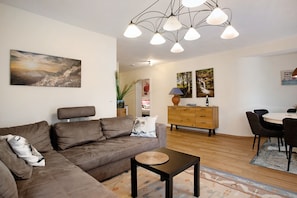 Un salon avec un canapé marron, une petite table, un coin repas avec des chaises et un meuble en bois.