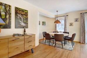 Un coin repas comprenant une table ronde, six chaises, un buffet en bois et deux tableaux accrochés au mur.