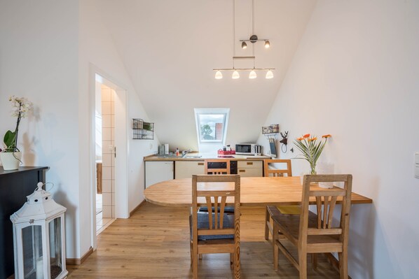 A modern kitchen with a wooden dining table, chairs, and a hanging light fixture.