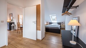 A bedroom with a bed, bedside table, lamp, and a view of the sky through a window.