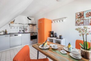 Et køkken med hvide skabe, et orange køleskab og et spisebord med stole.