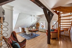 A loft-style room with a dining area, a cozy seating area, and a wooden staircase.