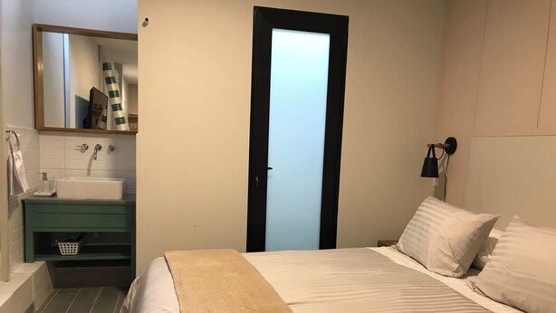 Ein Schlafzimmer mit Bett, Nachttisch, Waschbecken, Spiegel und Handtuchhalter.