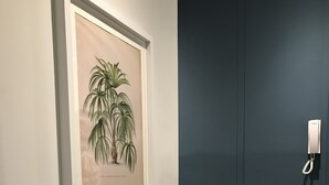 Ein gerahmtes Pflanzenblatt-Bild an einer Wand, eine Holzbank mit einem Zierpaneel und eine dunkelblaue Tür mit einem Telefon.