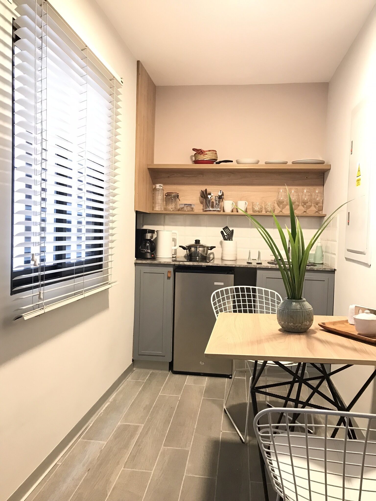A compact kitchen with a dining area, featuring a refrigerator, a coffee maker, and a potted plant on the table.
