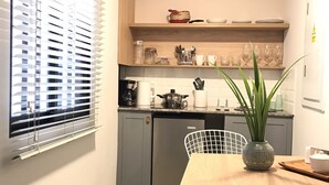 Eine kompakte Küche mit Essbereich, ausgestattet mit einem Kühlschrank, einer Kaffeemaschine und einem Blumentopf auf dem Tisch.