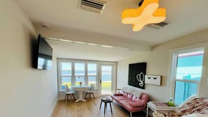 Un ampli saló amb una finestra gran que ofereix vistes al mar, un sofà rosa, una taula petita i un televisor de pantalla plana fixat a la paret.