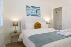 Un dormitorio con cama, dos mesitas de noche, una mesilla auxiliar, un cuadro en la pared y una puerta.