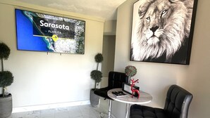 Ein modernes Wohnzimmer mit einem großen Fernseher, der eine Karte von Sarasota, Florida zeigt. Zwei schwarze Barhocker, ein kleiner runder Tisch mit einem Buch und einem roten Dekorationsobjekt sowie ein Blumentopf sind ebenfalls vorhanden.