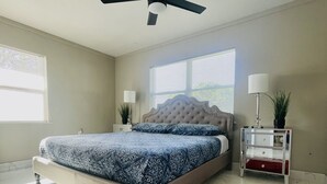Ein Schlafzimmer mit einem Bett, einem Deckenventilator, einem Nachttisch mit Lampe, einem roten Teppich und einem Fenster mit Jalousien.