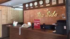 A reception desk with clocks displaying different time zones, a sign reading "Sea Side," and a phone. - Seaside Hotel (Incheon)