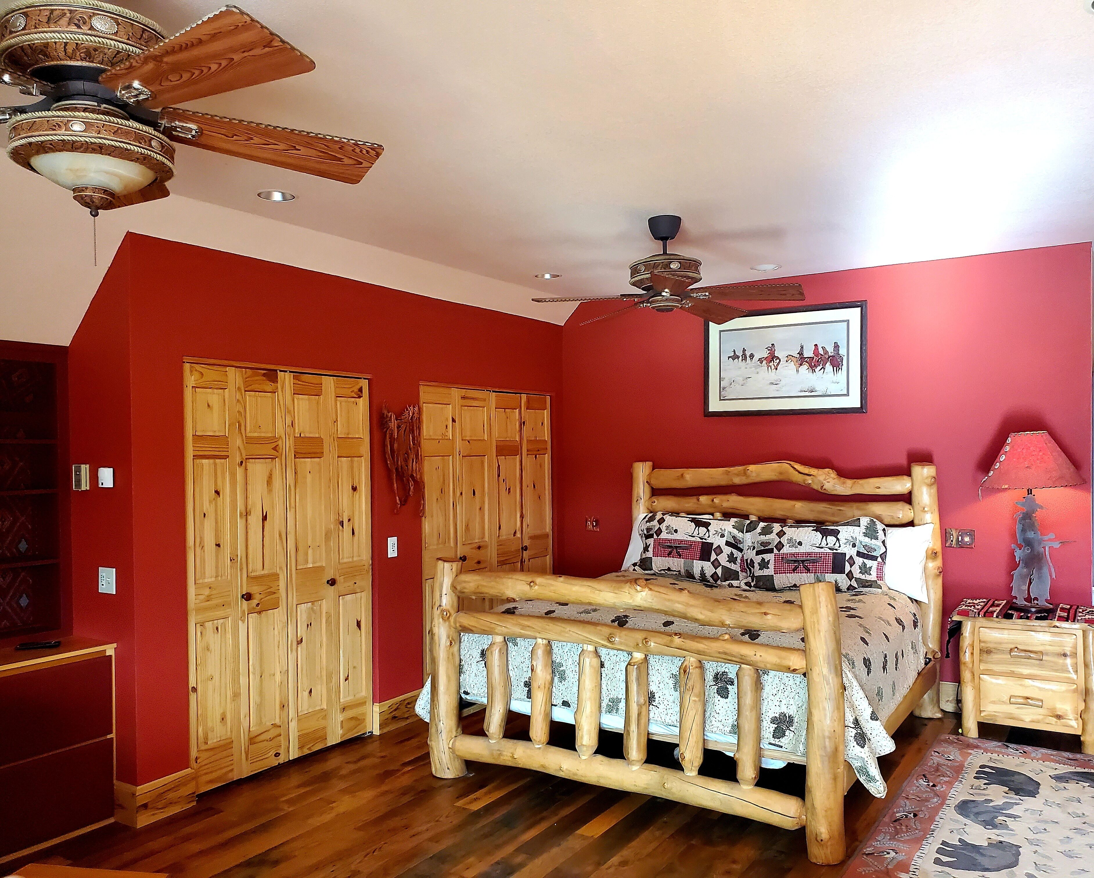 Una camera da letto con un letto di legno, una ventola a soffitto e una parete rossa.