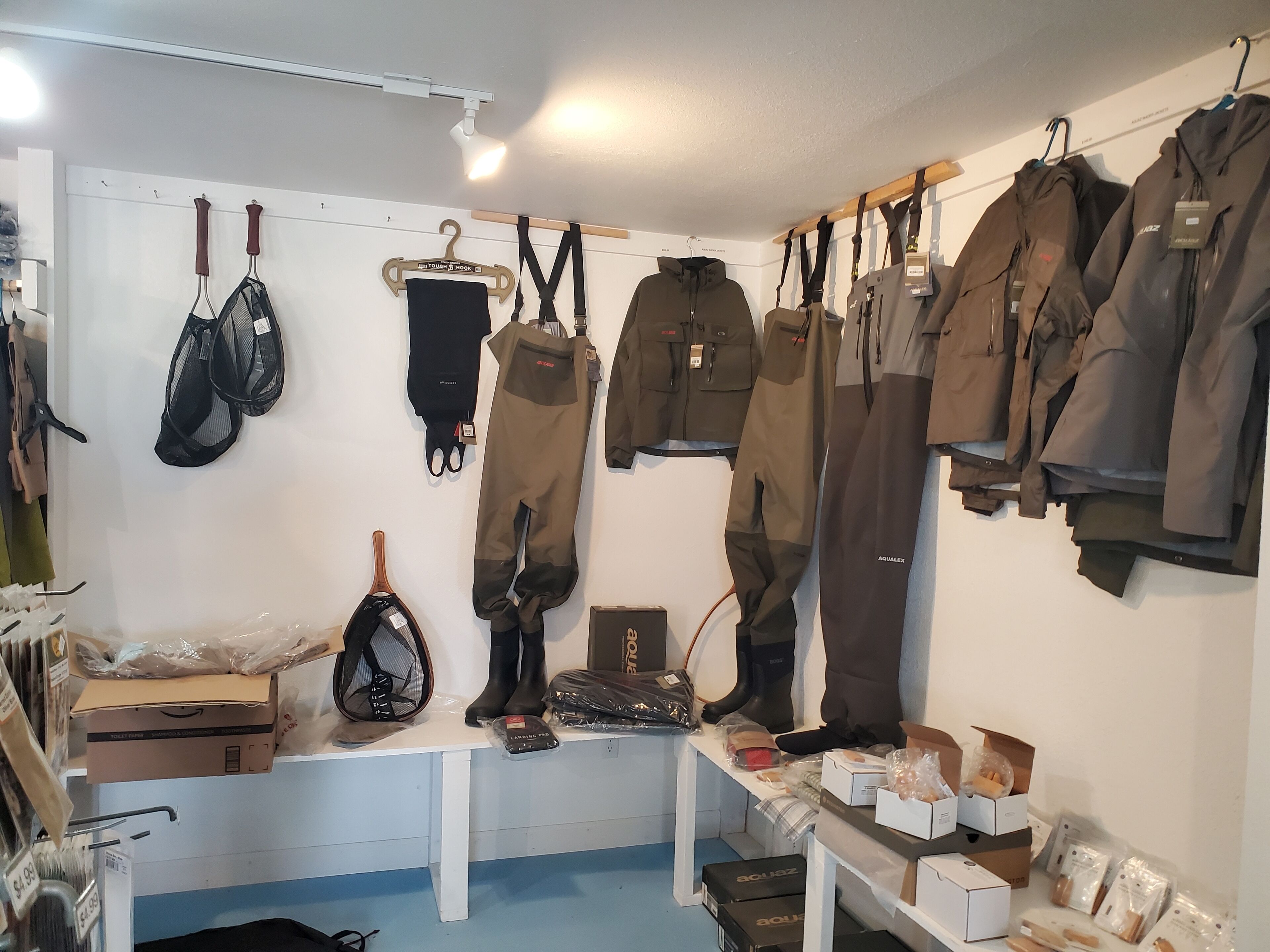 Una habitación con equipo de exterior diverso, como chaquetas, pantalones y botas, colgado en la pared y sobre una mesa.