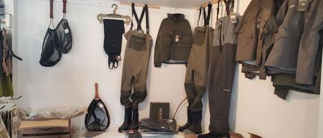 Una habitación con equipo de exterior diverso, como chaquetas, pantalones y botas, colgado en la pared y sobre una mesa.