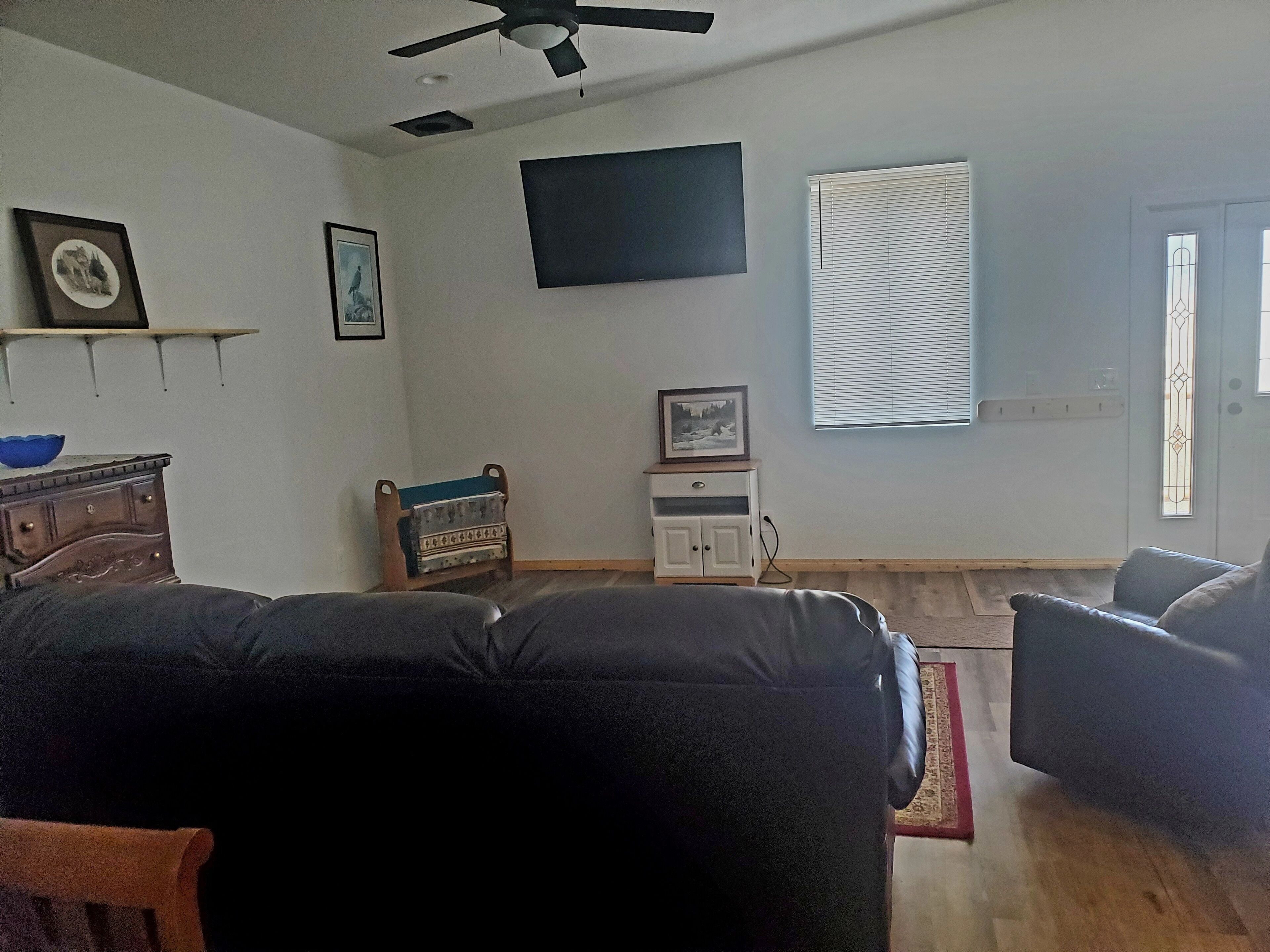 A living room with a black sofa, a wooden cabinet, a small table with a picture, and a window with blinds.